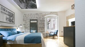 Een slaapkamer met een stenen muur, een bed met blauw beddengoed, een bureau en een stoel.