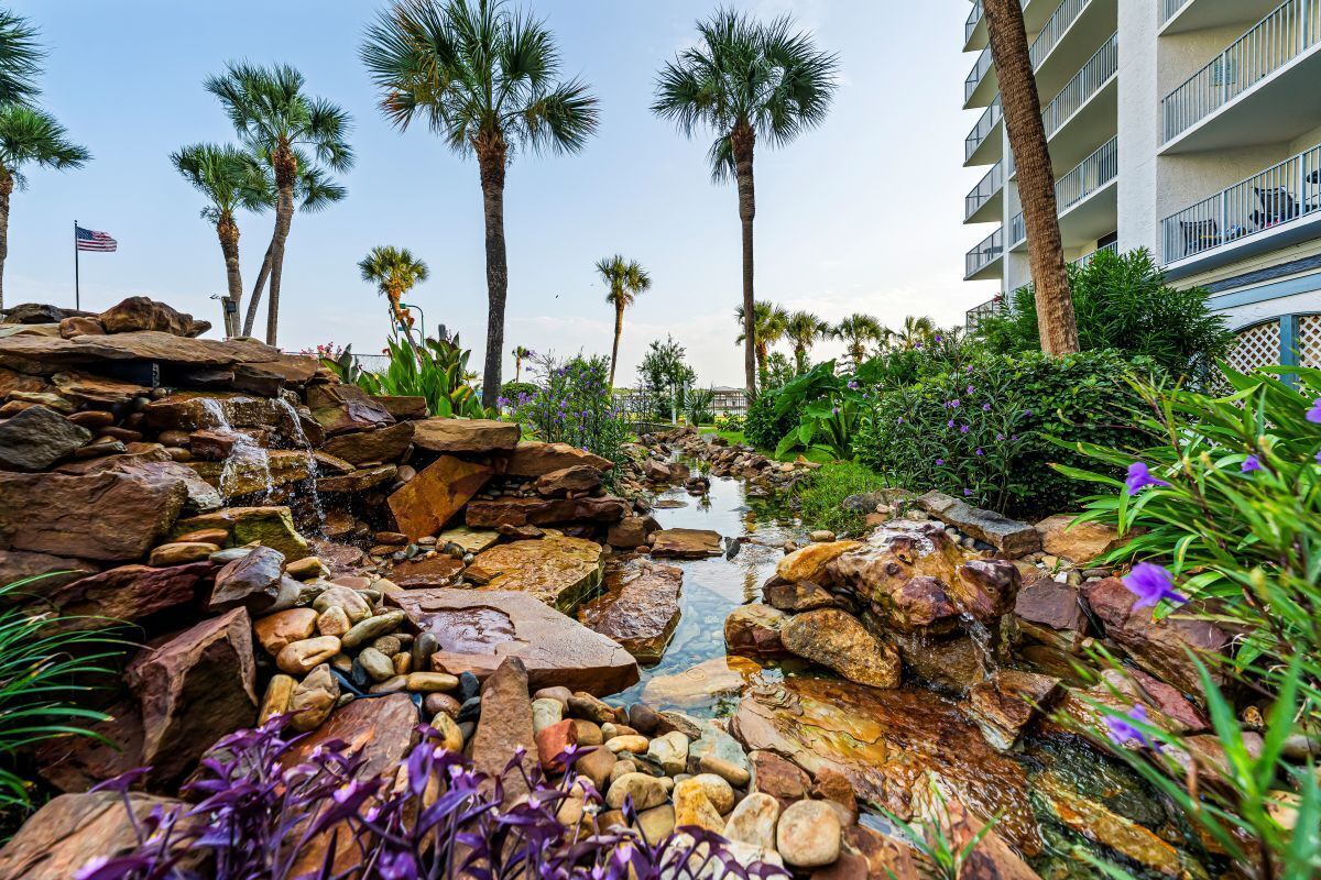 A landscaped area with a water feature, palm trees, and a building with balconies.