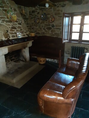 A stone-walled room with a fireplace, a leather sofa, and a window with a view. - Casa da Janal for 4 people (Vimioso)