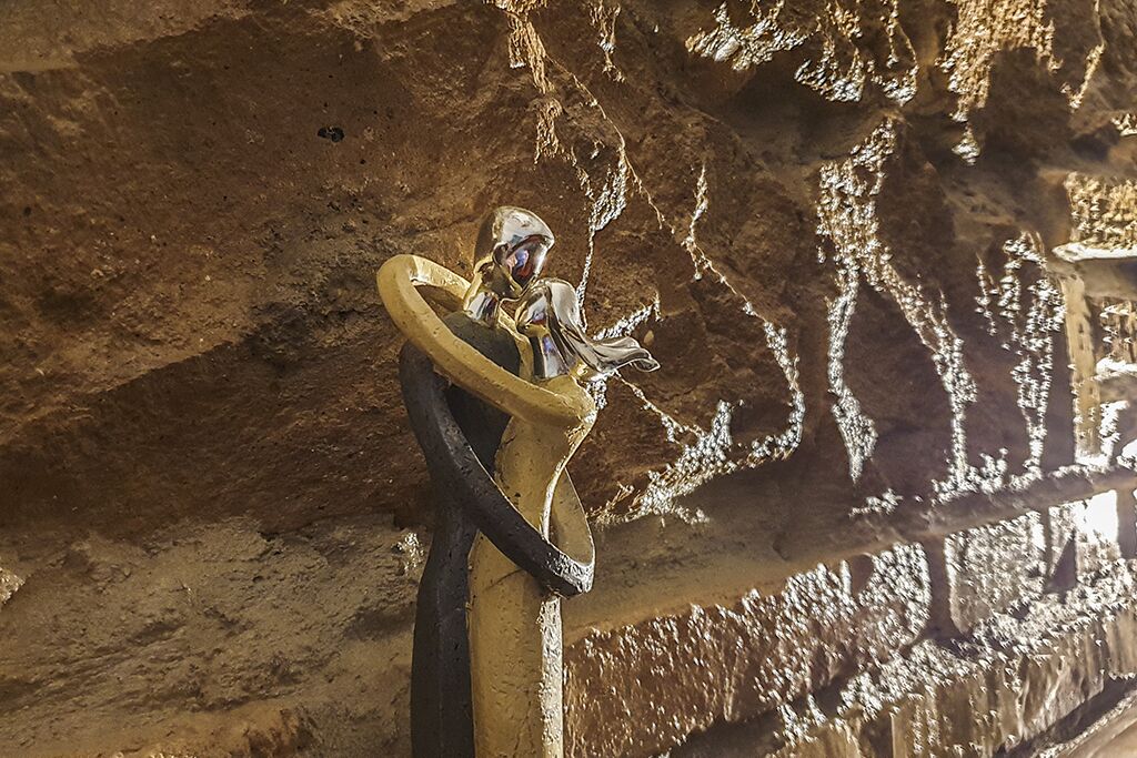 A cave interior with stalactites and stalagmites, a yellow metal structure, and a person wearing a helmet.
