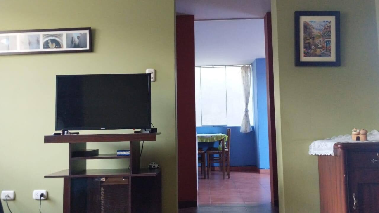 A room with a television on a wooden stand, a dining area with a table and chairs, and a cabinet with a decorative item on top.