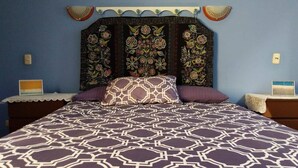 Une chambre à coucher avec une couvre-lit à motifs, une tête de lit décorative et une table de chevet avec une lampe.