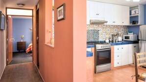 Un couloir mène à une cuisine équipée de meubles blancs, d’une cuisinière et d’un four à micro-ondes.