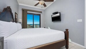 Ein Schlafzimmer mit einem großen Bett, einem Deckenventilator, einem Fernseher und Blick aufs Meer durch ein Fenster.