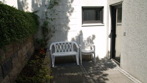 A small outdoor seating area with a bench and a chair, a stone wall, and a window. - Living comfortably in Oberwalluf, enjoying the Rheingau, experiencing the Rhine - Main! (Walluf)