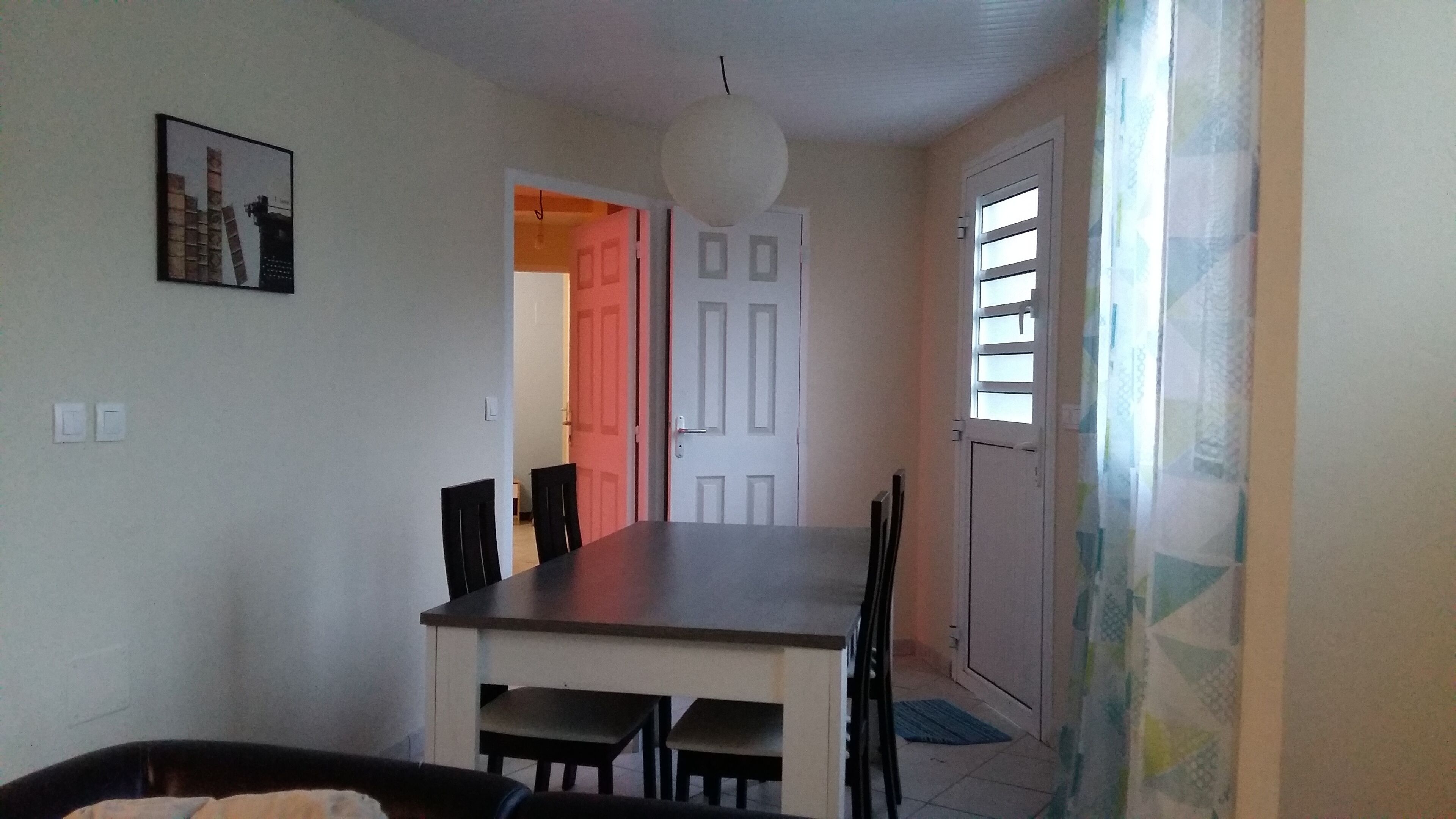 Un comedor con una mesa y sillas, una lámpara colgante y una puerta que da a otra habitación.