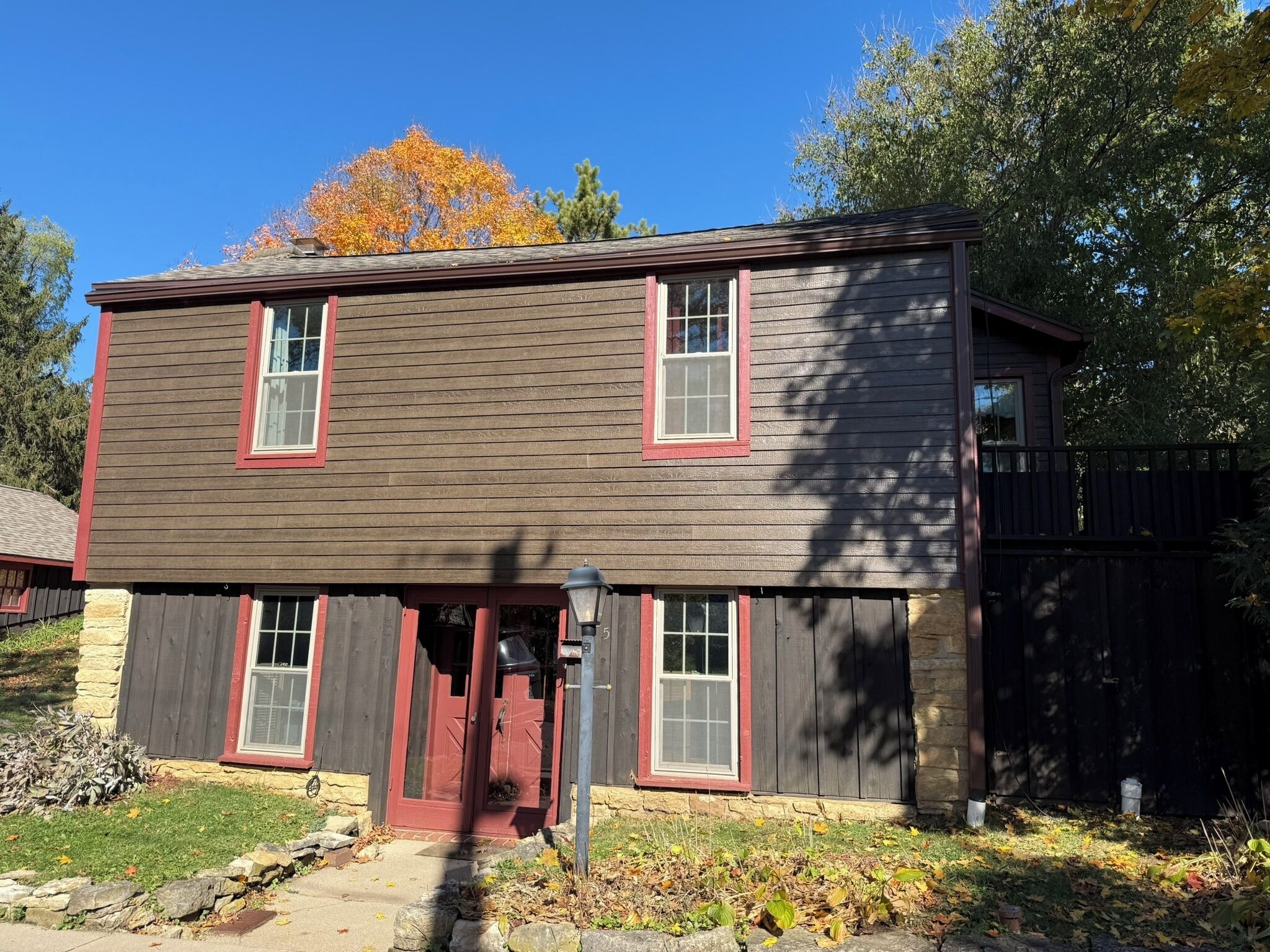 A two-story house with a stone foundation, red-framed windows, and a dark brown siding exterior.