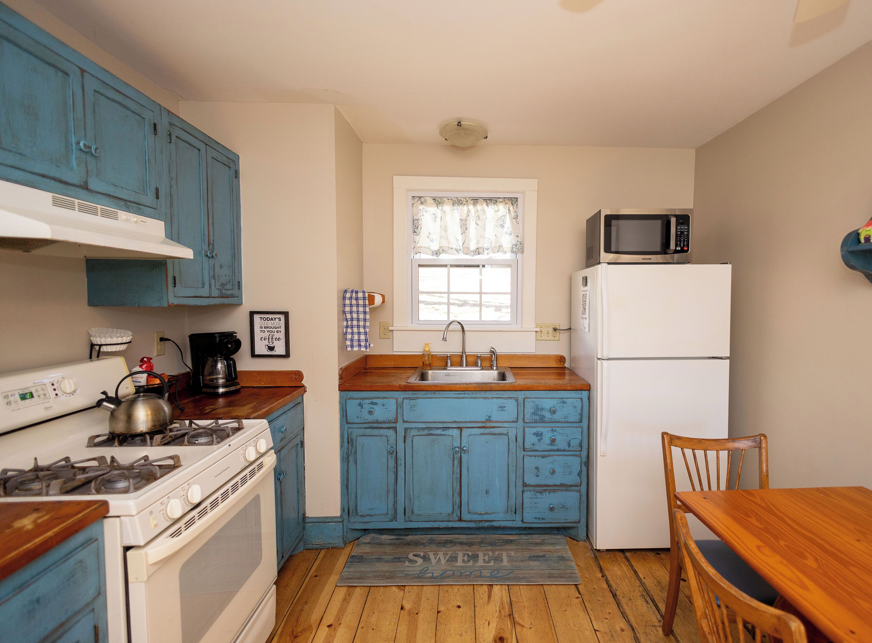 A compact kitchen with blue cabinets, a white stove, a sink, a microwave, and a refrigerator.