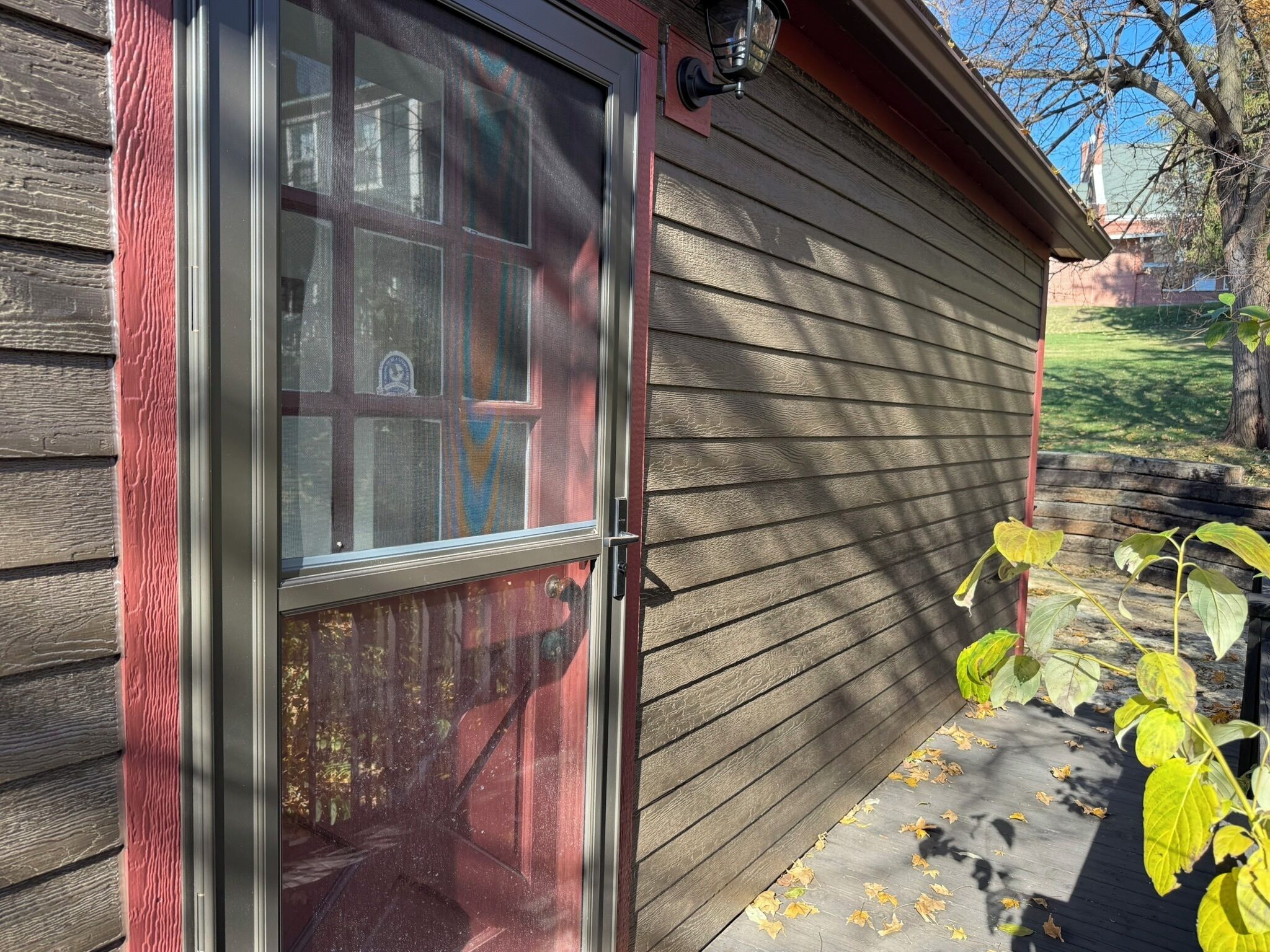 A wooden exterior with a sliding glass door, a small porch, and a leaf-covered ground.