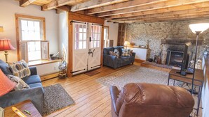 Ein gemütliches Wohnzimmer mit Kamin, Holzbalken, einer Couch und einem Fernseher.