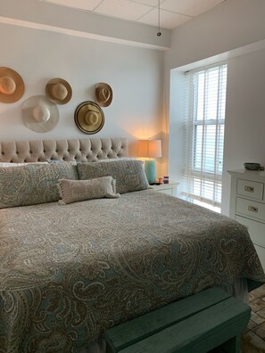 A bedroom with a tufted headboard, patterned bedding, and a bench. - Come stay at guest favorite-Salty Kisses on the Beach! (Pensacola Beach)