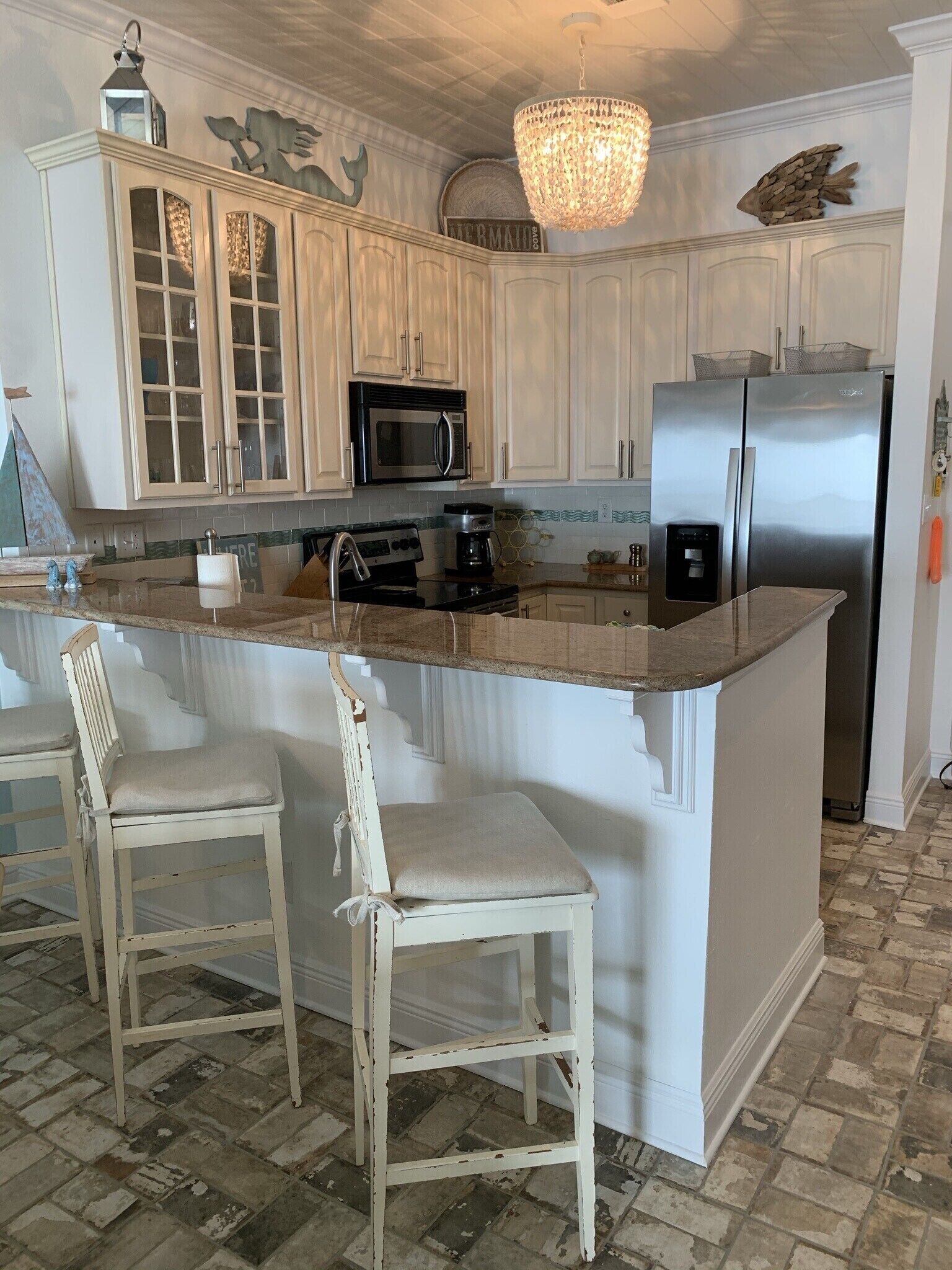 A kitchen with white cabinetry, a central island with bar stools, a stainless steel refrigerator, and a chandelier.