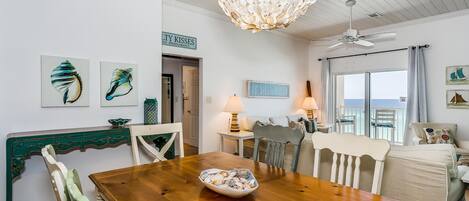 Un comedor con mesa de madera, sillas y una lámpara de araña. Se observan obras de arte en las paredes y un letrero que indica la ubicación.