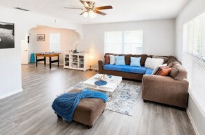 A living room with a sofa, ottoman, coffee table, and a ceiling fan.