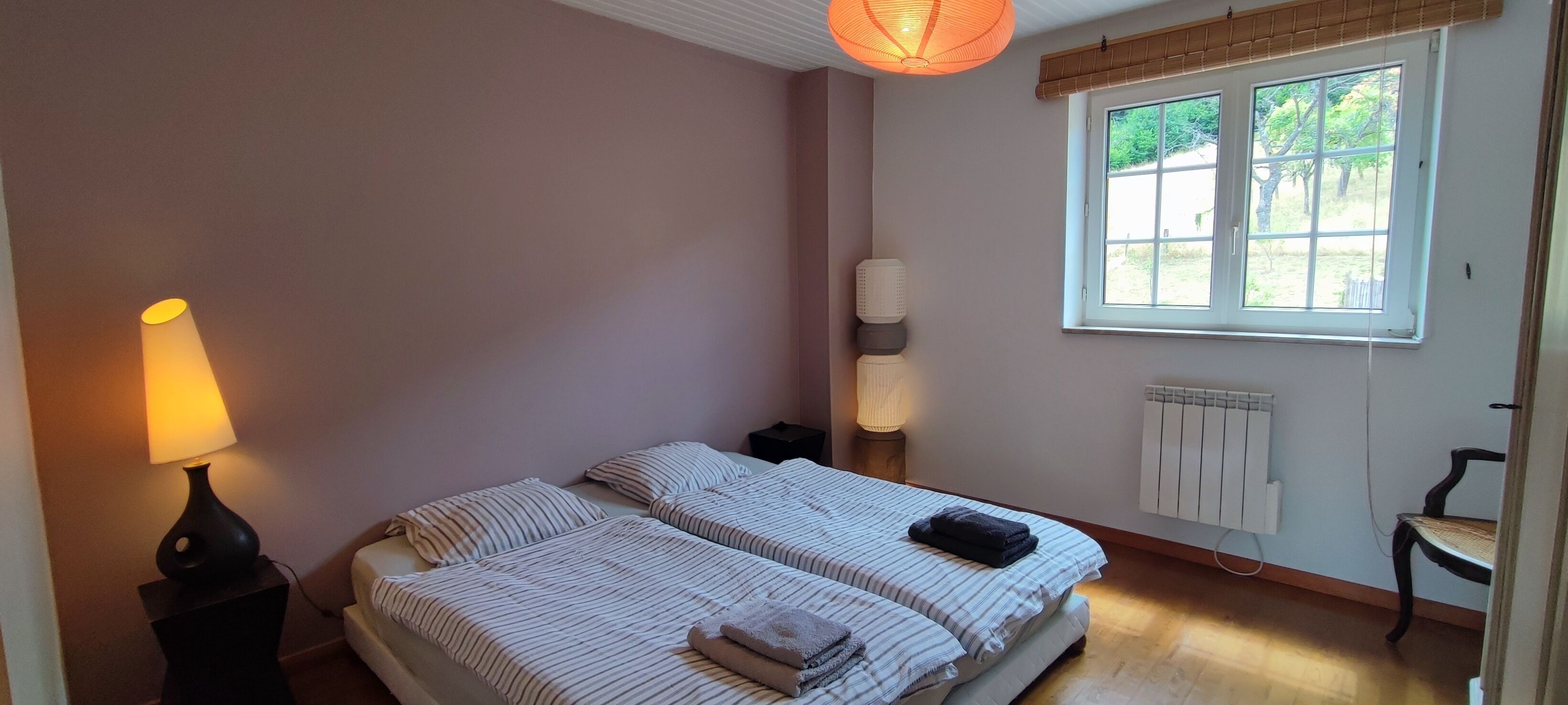 A bedroom with two beds, a bedside table, a lamp, a window, and a radiator.