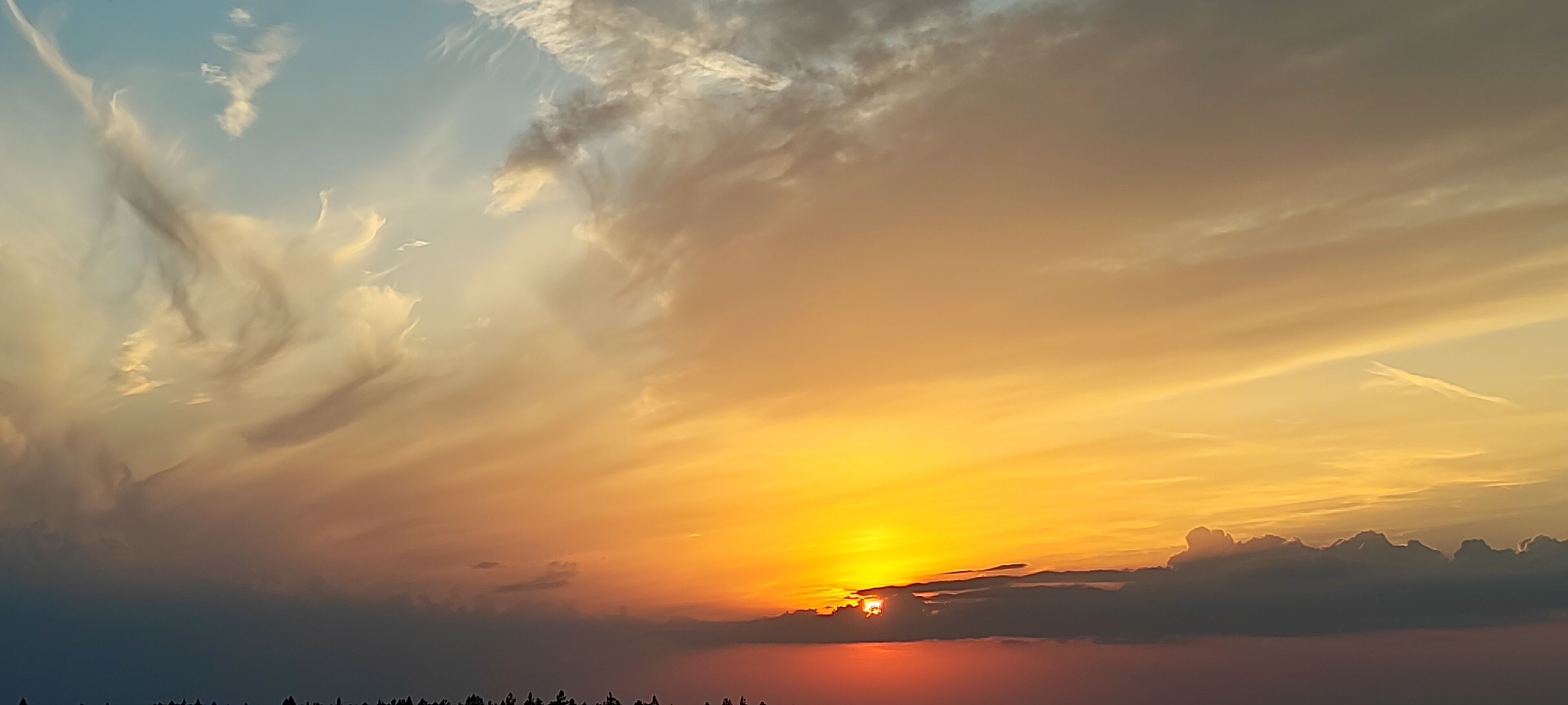 Un coucher de soleil avec des nuages et les silhouettes de montagnes.