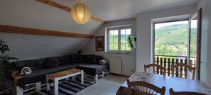 A cozy living room with a sofa, a wooden table, and a view of a lush landscape through a window.