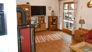 A cozy living room with a fireplace, wooden furniture, a flat-screen TV, and a window with curtains. - Nice holiday home "Aunt Emma" in Regen, Bavarian Forest, pets welcome (Kattersdorf)