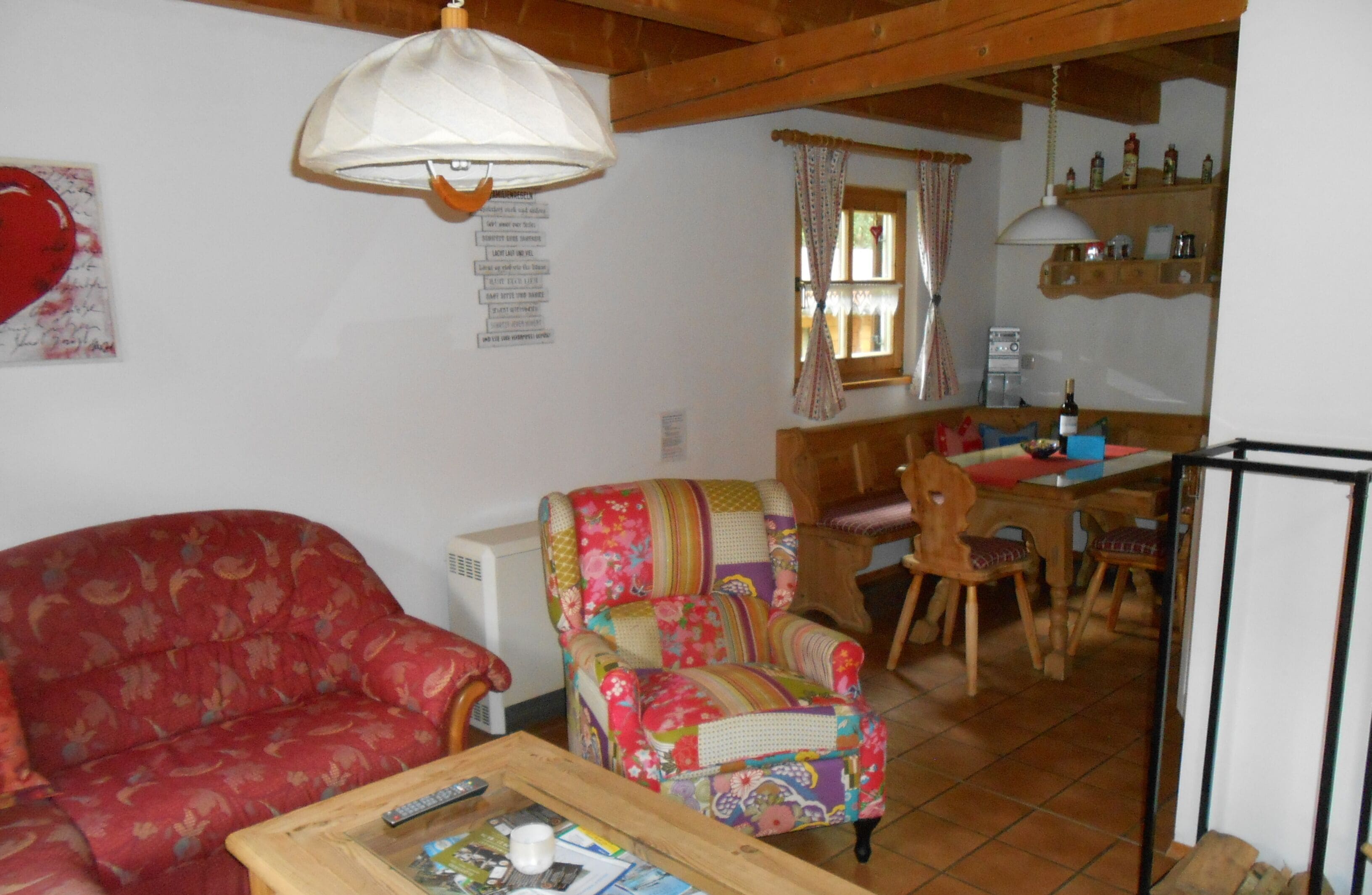 Una sala de estar con un sofá rojo, un sillón colorido, una mesa de centro de madera y un comedor con una mesa y sillas de madera.