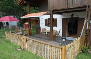 A wooden deck with a covered seating area, a fenced garden, and a small red building in the background. - Nice holiday home "Aunt Emma" in Regen, Bavarian Forest, pets welcome (Kattersdorf)