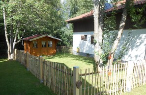 A wooden cabin with a red roof, surrounded by a wooden fence and trees. - Nice holiday home "Aunt Emma" in Regen, Bavarian Forest, pets welcome (Kattersdorf)