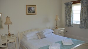 A neatly made bed with white linens and a green accent, a bedside table with a lamp, and a window with curtains. - Brock Cottage private Hot Tub DOG/Cat FRIENDLY* with on site fishing (Pickering)