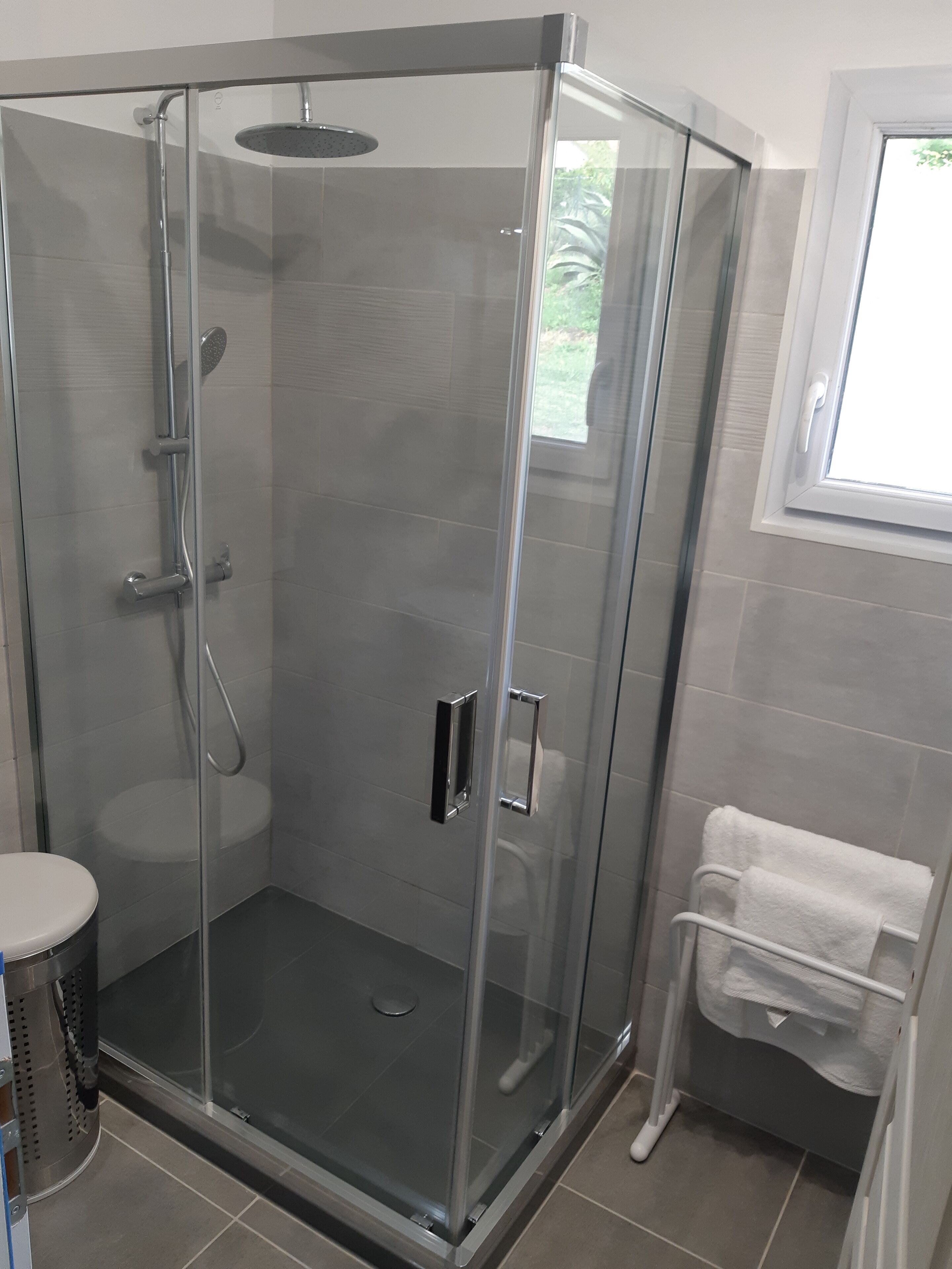 A glass-enclosed shower stall with a handheld showerhead, a handheld shower head, and a wall-mounted faucet.
