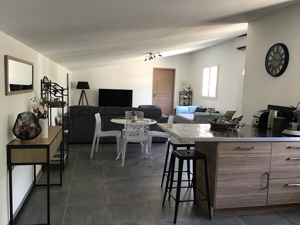 Una cocina moderna con una isla central, taburetes de bar, una mesa de comedor y un sofá en la sala de estar.