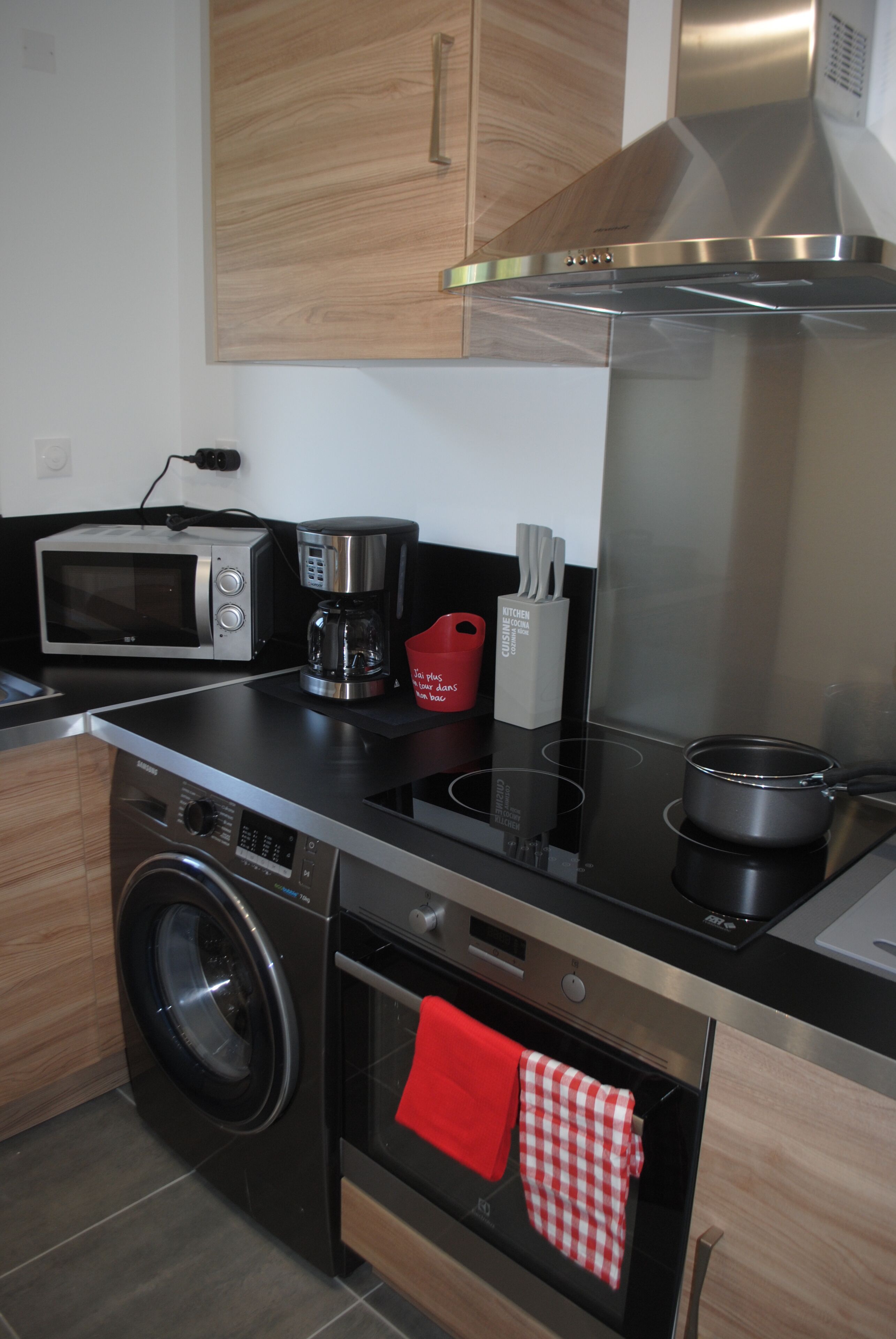 A modern kitchen with stainless steel appliances, a washing machine, and a red towel hanging on the oven door.