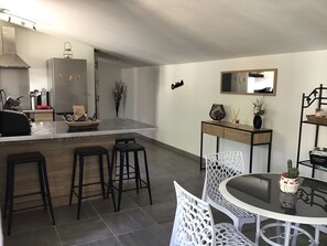Una cocina moderna con una isla central, taburetes de bar, una mesa de comedor con sillas y una mesita auxiliar con objetos decorativos.