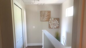 Un corridoio con pavimento in legno scuro, pareti bianche e una reception con scrivania bianca. Si notano due elementi decorativi a parete e una bocchetta di ventilazione al soffitto.