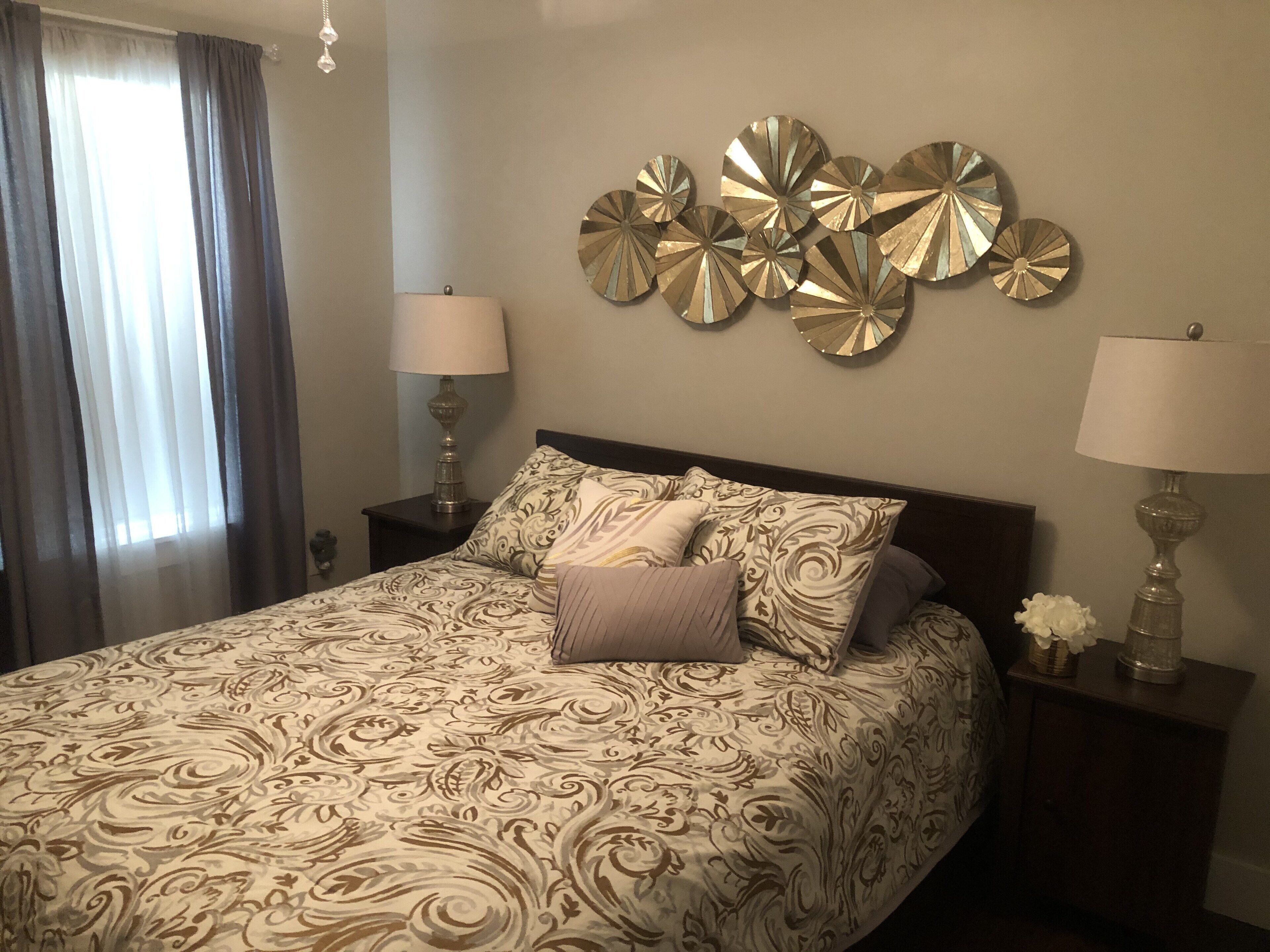 A hotel room with a large bed, two bedside tables with lamps, a decorative wall piece, and a window with curtains.