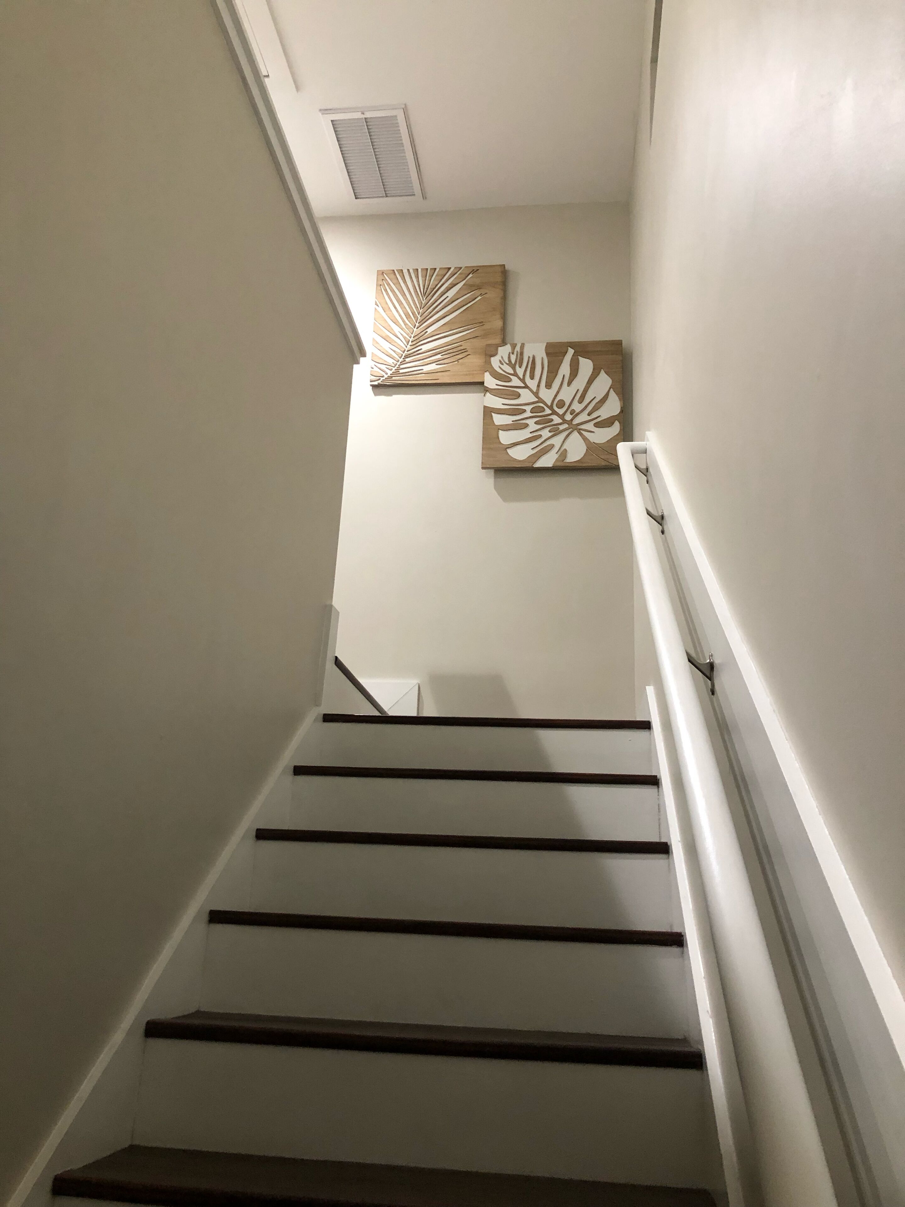 A staircase with wooden steps and white handrails, leading to a landing with two wall-mounted decorative pieces.