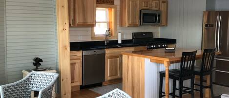 A kitchen with wooden cabinets, a stainless steel refrigerator, a microwave, and a sink. There are wicker chairs and a dining table.