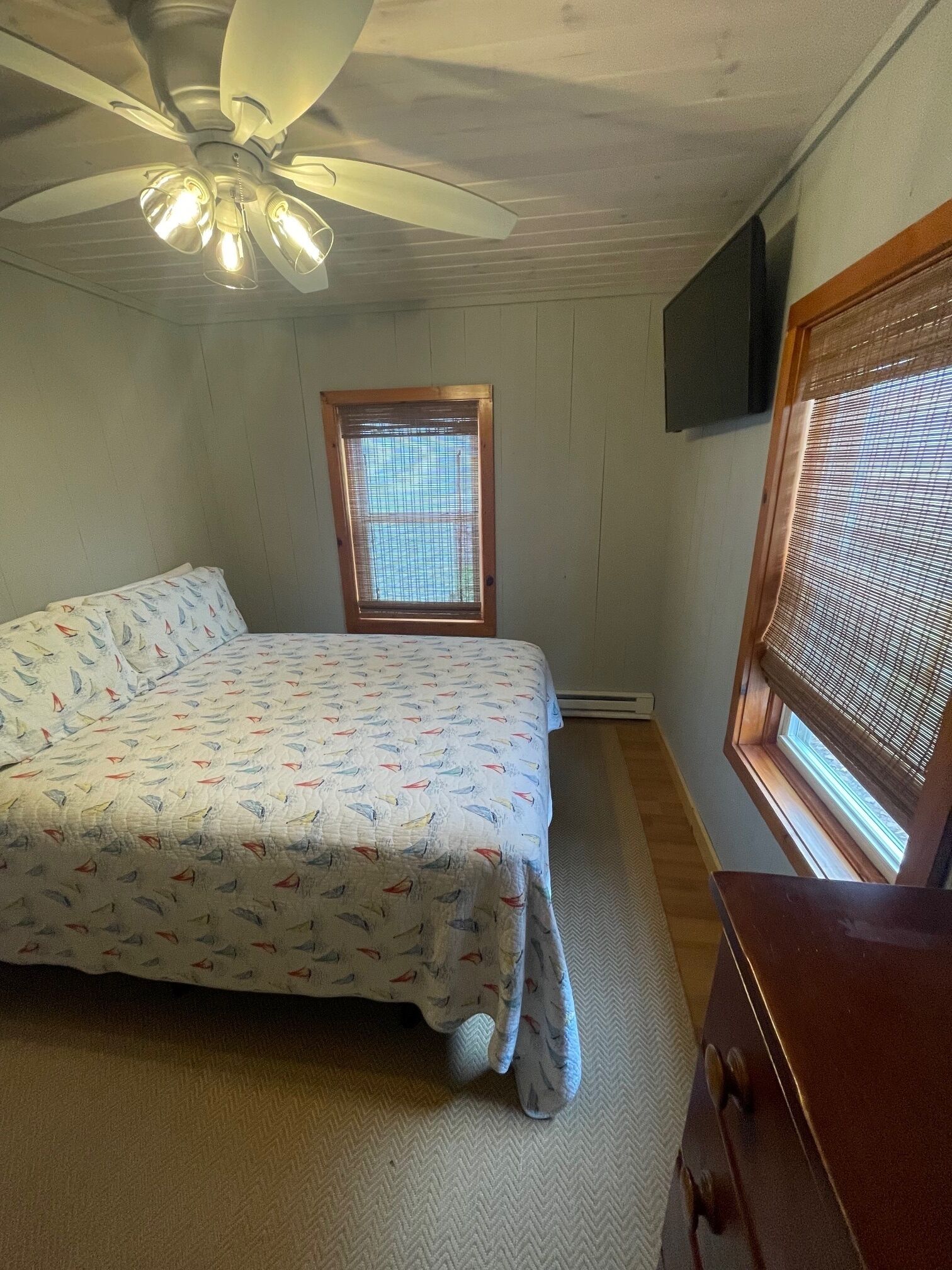 A bedroom with a bed, a ceiling fan, a window with blinds, and a TV mounted on the wall.