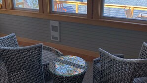 Une pièce meublée de mobilier en osier, avec une table en verre et de grandes fenêtres donnant sur un plan d’eau.