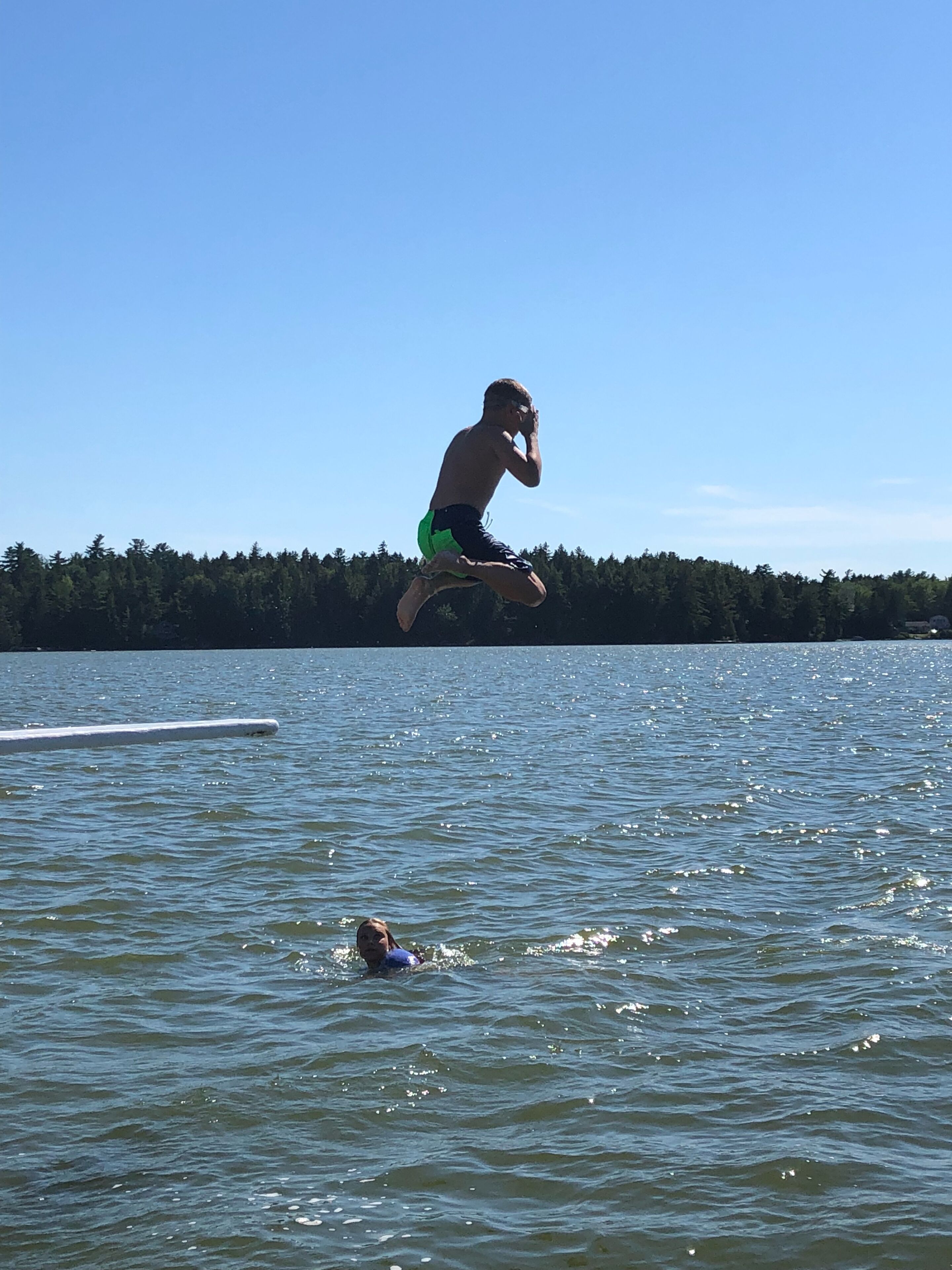 A person jumping into a lake with a forest in the background.