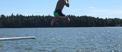 A person jumping into a lake with a forest in the background.