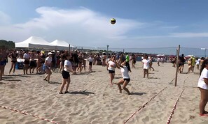 A crowded beach with people playing volleyball.