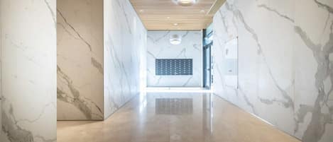 A modern hallway with marble walls and a polished floor, leading to a room with a wooden ceiling and a circular light fixture.
