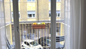 A balcony with a metal railing, a potted plant, and a view of parked cars and a building in the background. - Lovely bright apartment, with modern design, perfect for families! (Bolzano)