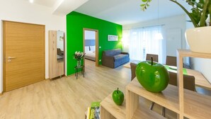A modern living room with a green accent wall, wooden flooring, a sofa, a dining table, and a green apple sculpture. - Lovely bright apartment, with modern design, perfect for families! (Bolzano)