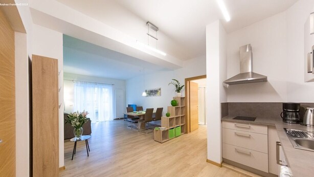 A modern kitchen with a stainless steel range hood, wooden cabinets, and a dining area with a table and chairs. - Lovely bright apartment, with modern design, perfect for families! (Bolzano)