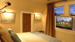 A bedroom with a bed, a desk, a chair, a television, and a window with curtains.