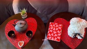 Un lit avec une couverture à motifs de cœur, une petite table avec une théière et un objet décoratif sur la table de chevet.