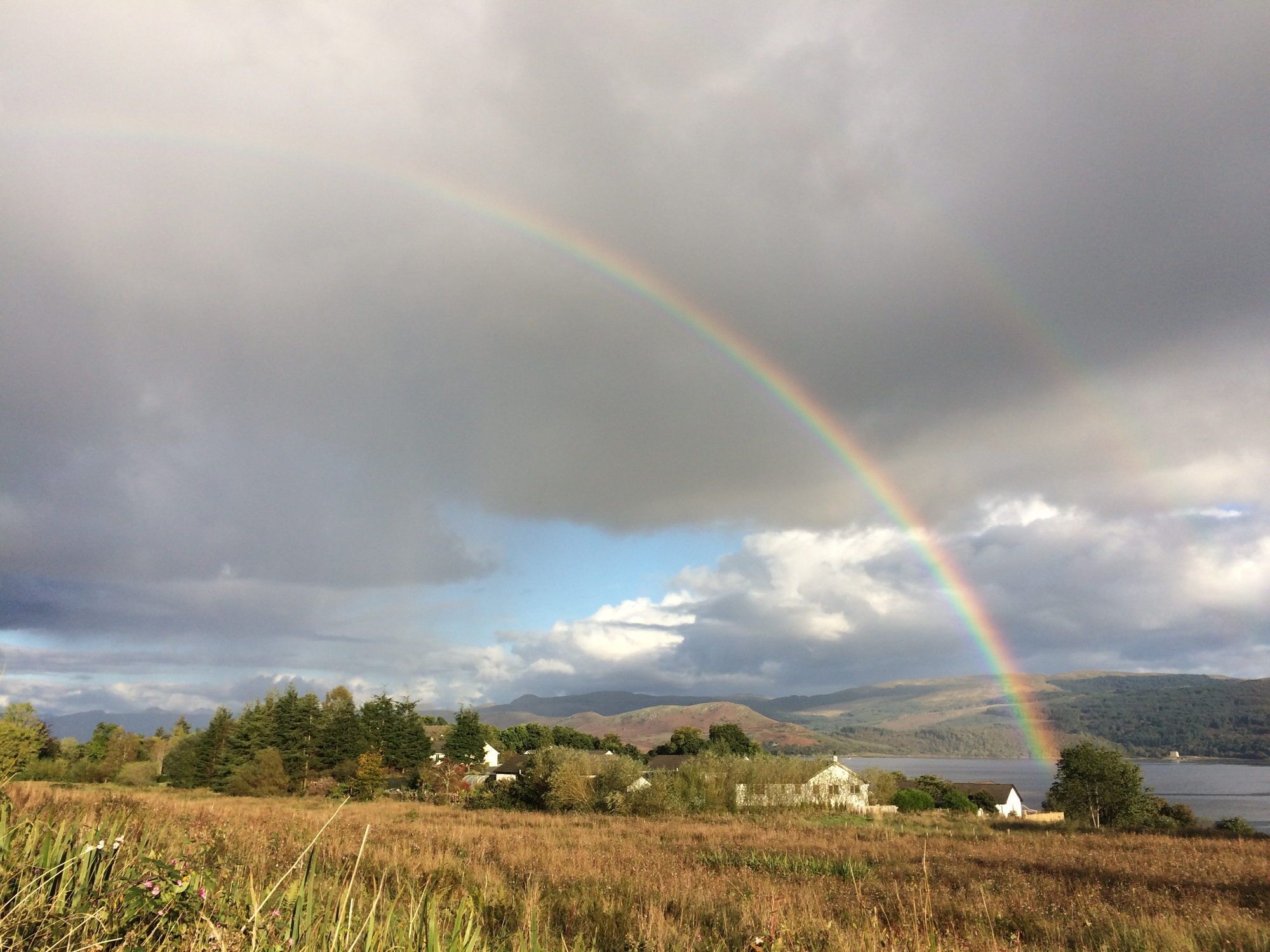Un paysage rural avec un arc-en-ciel, des maisons et un lac.