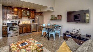 A modern kitchen with stainless steel appliances, a dining area with a table and chairs, and a flat-screen TV mounted on the wall. - Athlete, Family, and Pet Friendly - Something for everyone! (St. George)