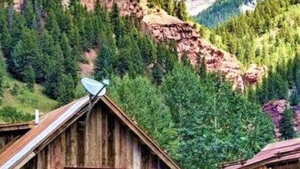 A rustic wooden cabin with a satellite dish, surrounded by lush greenery and mountains. - AUGUST SPECIAL! Luxury home-Heart of Telluride 3B+loft; deck/VIEWS/gas fireplace (Telluride)