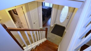 Eine Treppe führt zu einem Schlafzimmer mit einer Tür, einem Fenster mit Rollläden und einem kleinen Teppich am Fuß.