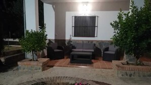 Un espace extérieur aménagé avec un canapé et des fauteuils, entouré de plantes en pot et d’un parterre de fleurs.